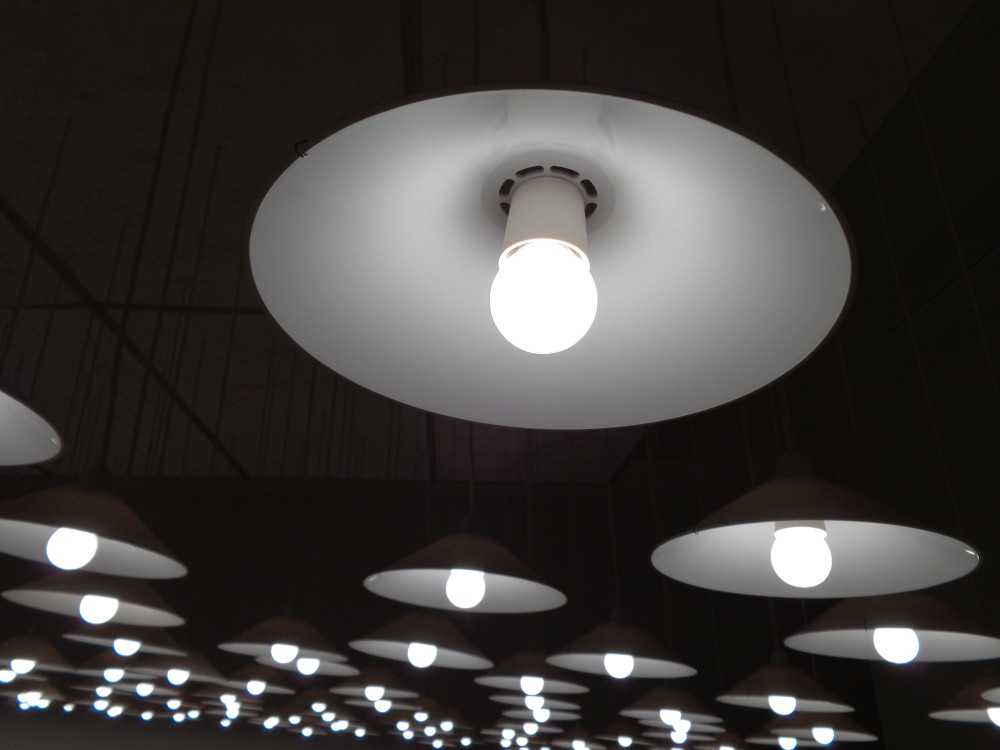A close up detail of one of the light fixtures as described in the image above. The light is black, circular and has a single glowing white bulb in the middle.