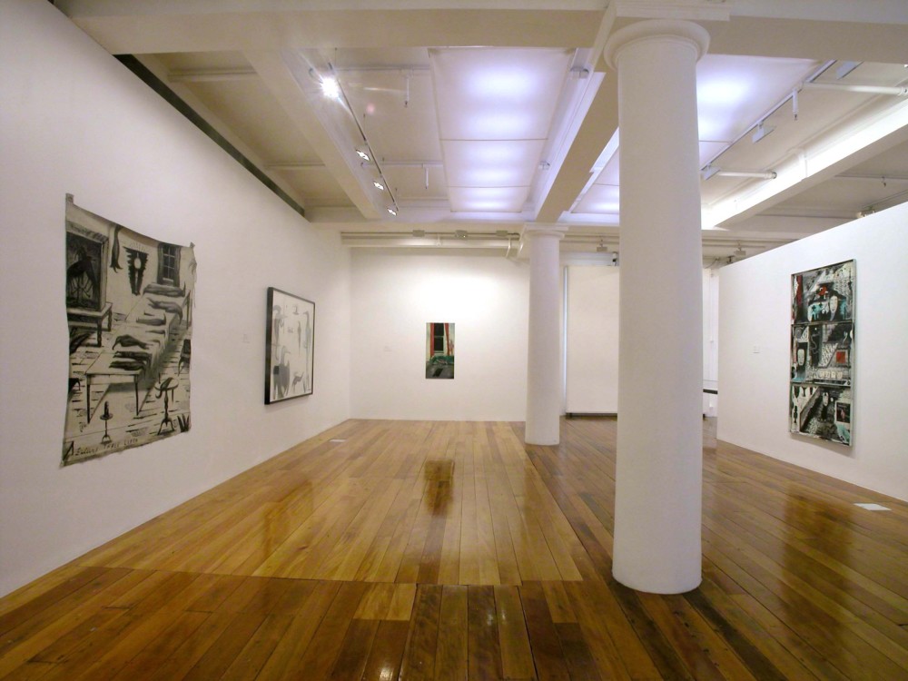 The image shows a white gallery space with a polished wooden floor. Two white columns are in the centre of the room, stretching from floor to ceiling. On the left hand wall hangs a large square artwork which depicts a scene inside a home. An oblong table holds stylised birds of varying sizes and lengths stacked neatly in rows, while three more hang in a clump from the ceiling. Two taxidermied huia birds, with long beaks, are perched stiffly in a large glass vitrine to the left of the table. A glowing lamp and window looking out into a dark night are also present in the work. Across the bottom, the title of the painting, 'Buller's Tablecloth' is written in capital letters. To the right of this painting, another work can just been seen in a large horizontal black frame. This work is also filled with multiple, humanoid birds with long beaks and human arms and hands. Some have wings extending out of their backs, like angels. All are looking in different directions. On the back wall of the gallery hangs a tall vertical painting which depicts a living room space. On a green couch in the living room a young woman (who has one leg and one tail, appearing to be a hybrid mermaid of some sort) lies asleep on the couch, while a tall man covered in red veins sneaks along the back of the couch towards the open window looking into a dark night, with what looks like a gun in his hand. On the far right wall of the gallery is a large horizontal work which is divided into three sections. Japanese imagery, including calm Noh theatre masks, manga-inspired figures and objects, curved dragons, bonsai trees and crowds make up each of the scenes in this artwork. 
